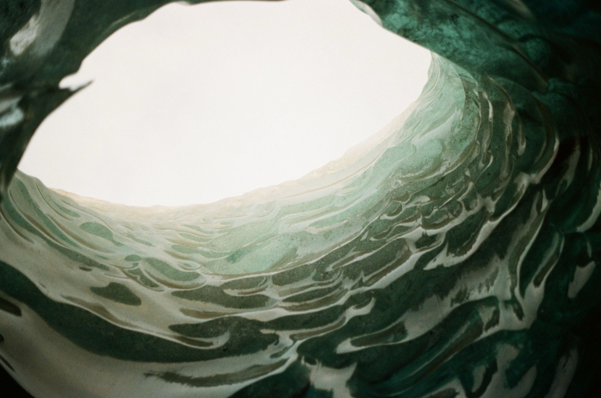Film photograph looking up through an opening in rippled green ice